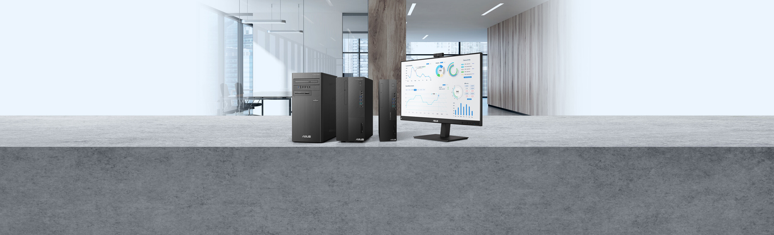 L'immagine mostra due computer desktop neri e un monitor. Il monitor sta visualizzando un'interfaccia con grafici e tabelle. Lo sfondo sembra essere un ambiente d'ufficio moderno, con ampie finestre e pareti luminose.