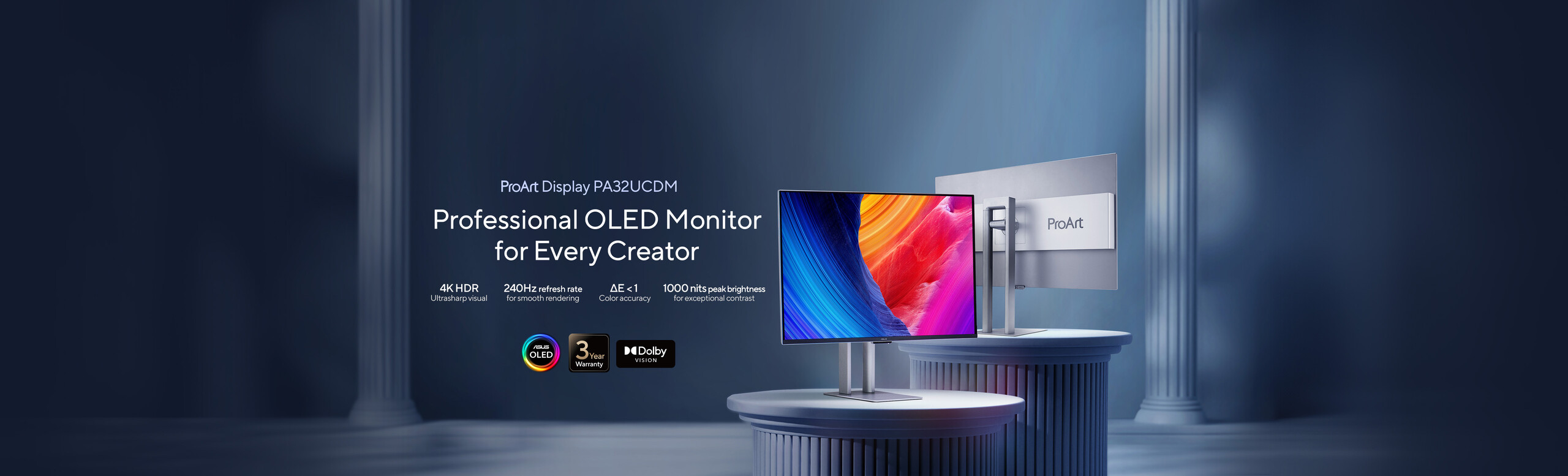 Two sleek ProArt OLED monitors displayed on elegant round pedestals with colorful abstract graphics. Background features grand columns, creating a professional and artistic ambiance.