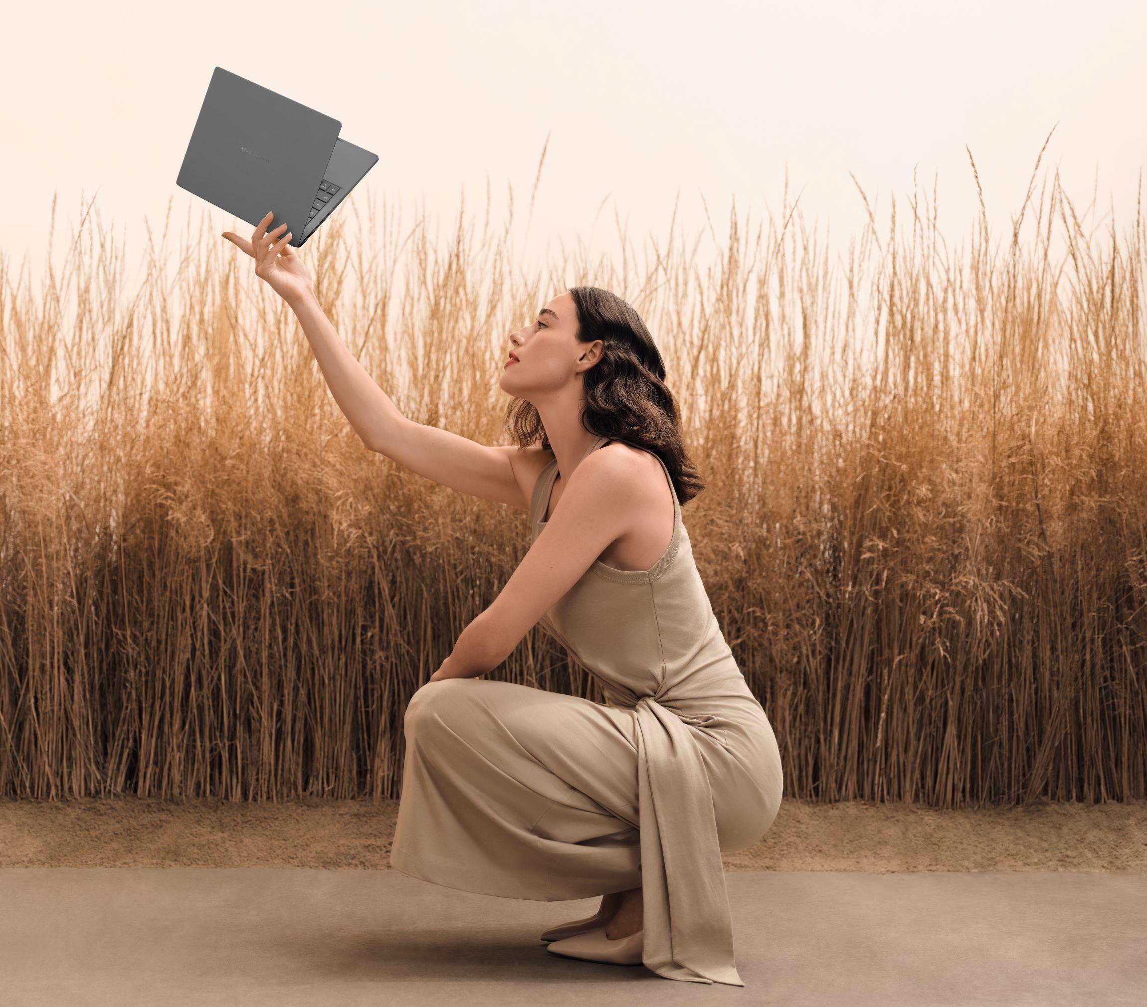 A woman in a field of wheat shown efortlessly holding an ASUS Zenbook A14 using only her fingertips
